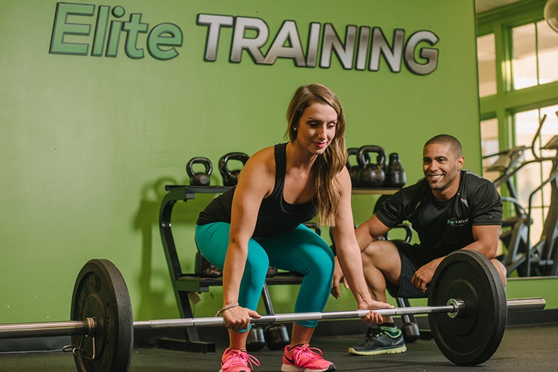 Woman lifting weights with a personal trainer at Elite Training's Tulsa Location